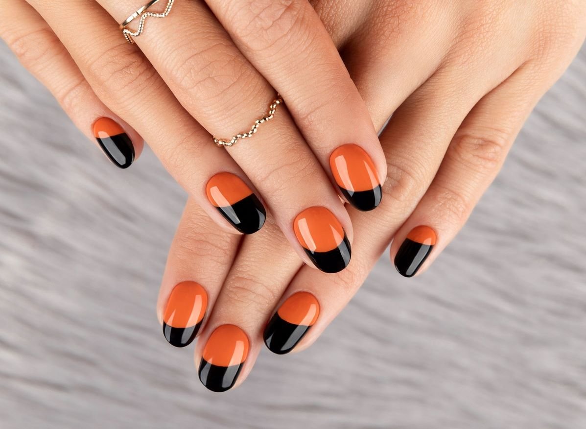 Zwei Hände mit schwarz-orange lackierten Fingernägeln und silbernen Ringen vor einem grauen Hintergrund