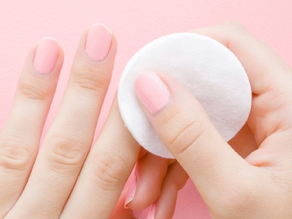Person entfernt rosa Nagellack an den Fingern mit einem Wattepad