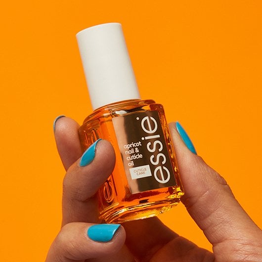 Hand mit blauer Maniküre, die essie apricot nail & cuticle oil im klassischen Format hält