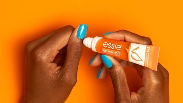 Hände einer Person mit blauer Maniküre, die on a roll cuticle oil auf ihre Nagelhaut aufträgt